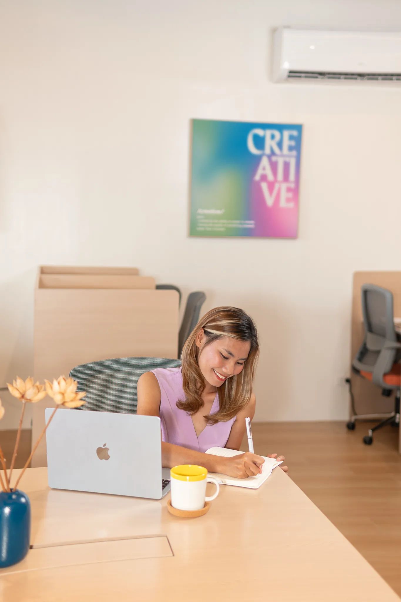 A woman writing notes while working on a laptop inside Mangoes and Bananas coworking space.