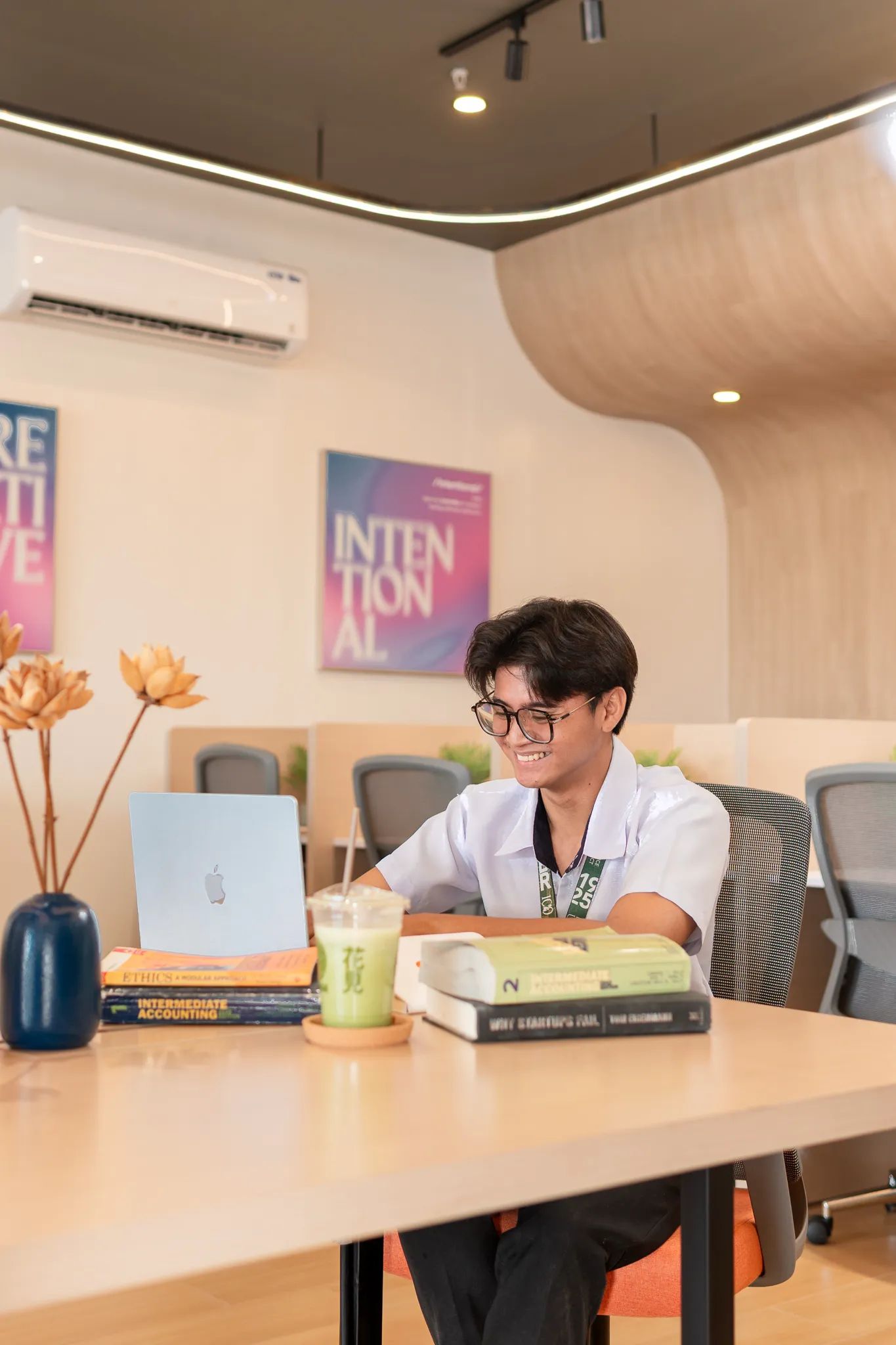 Student working on a laptop with books inside Mangoes and Bananas coworking space.